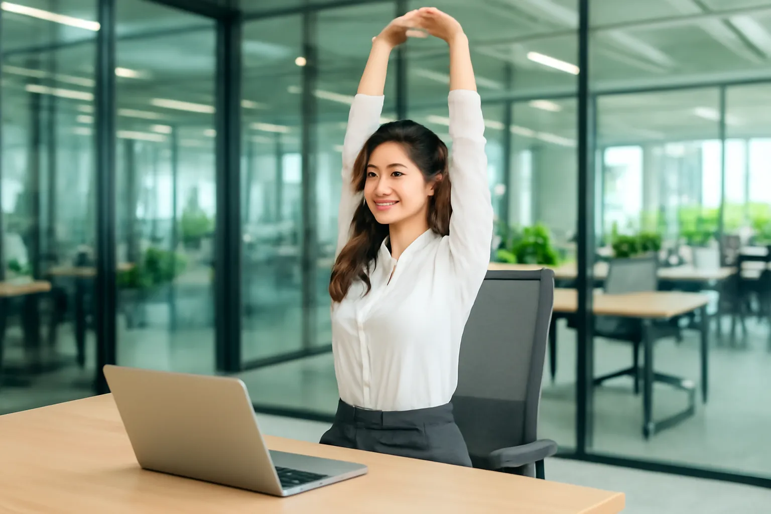 Nữ nhân viên đứng dậy duỗi lưng bên bàn làm việc trong văn phòng cửa kính